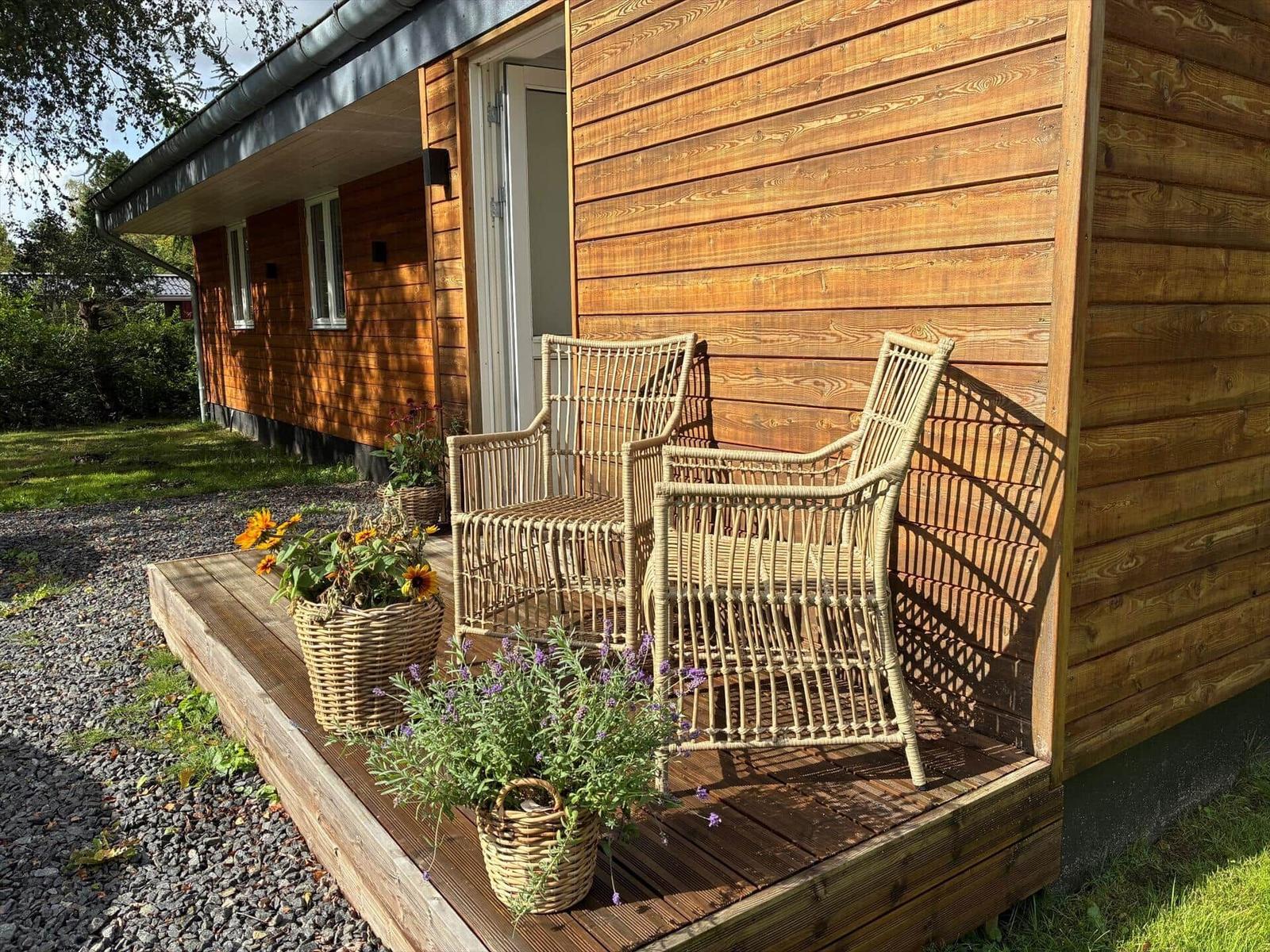 Wooden deck with two wicker chairs and flower baskets in front of a wooden house.