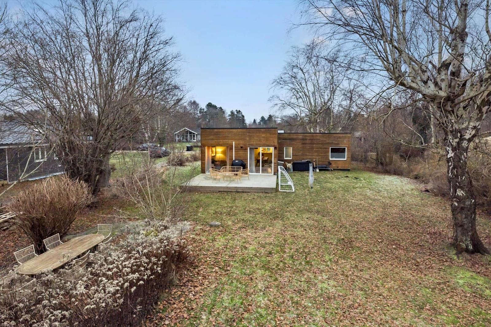 Modern wooden cabin with terrace, garden, and trees in the background.
