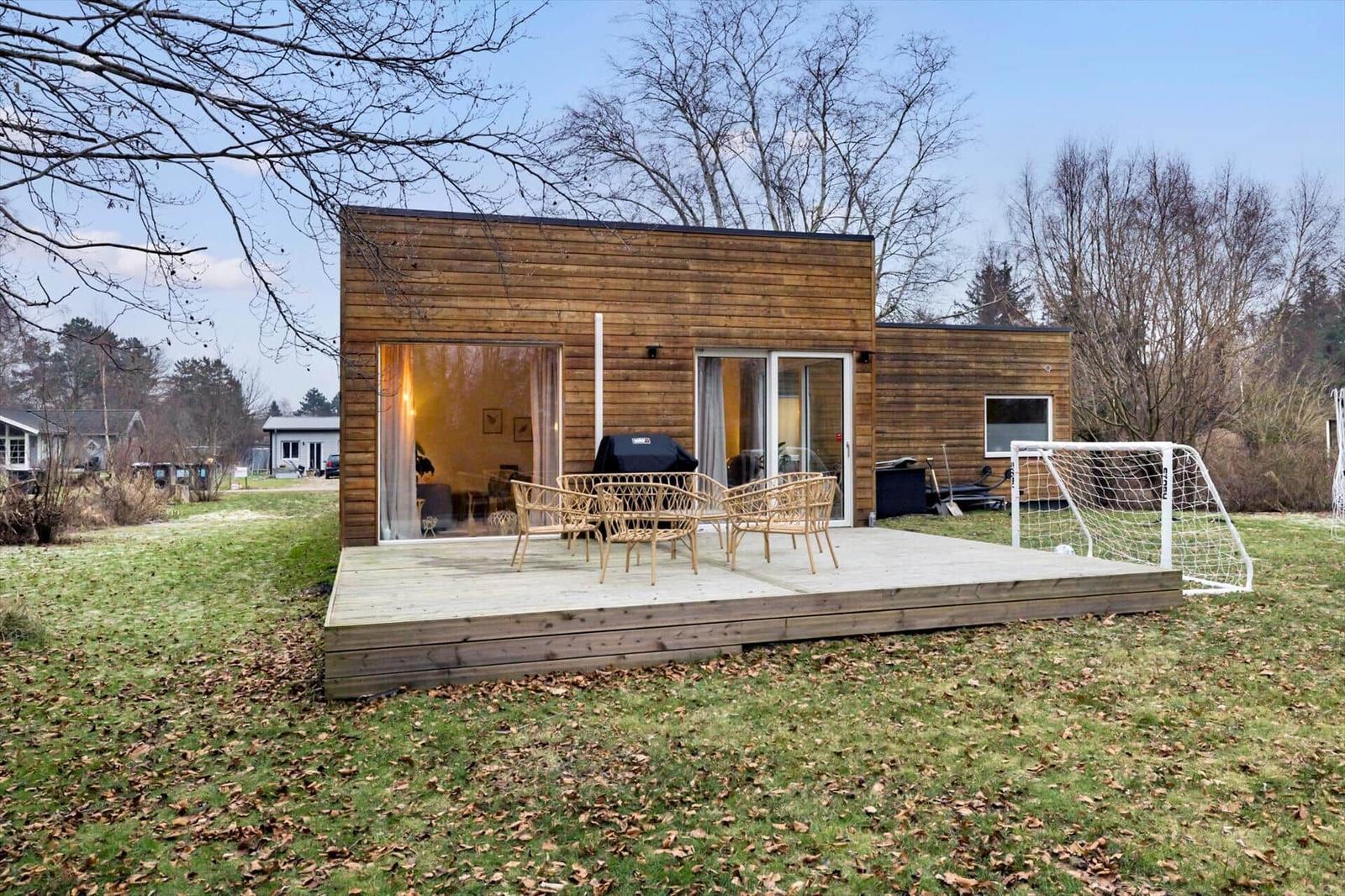Modern wooden cabin with deck, grill, and soccer goal in the yard.