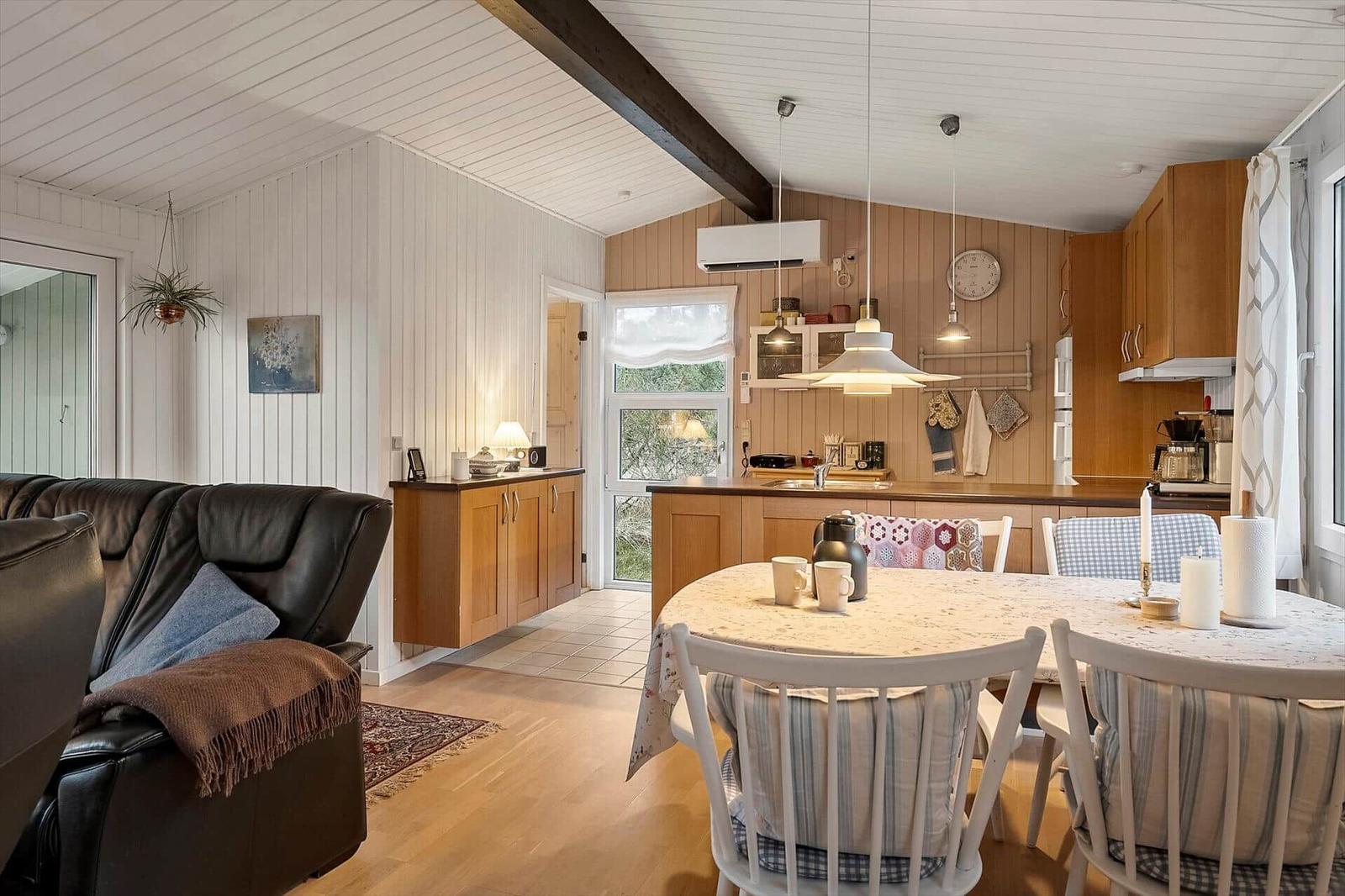 Wohnbereich mit Essbereich und Küche. Holzdecke, Sofa, Tisch mit Stühlen und Küchenzeile.