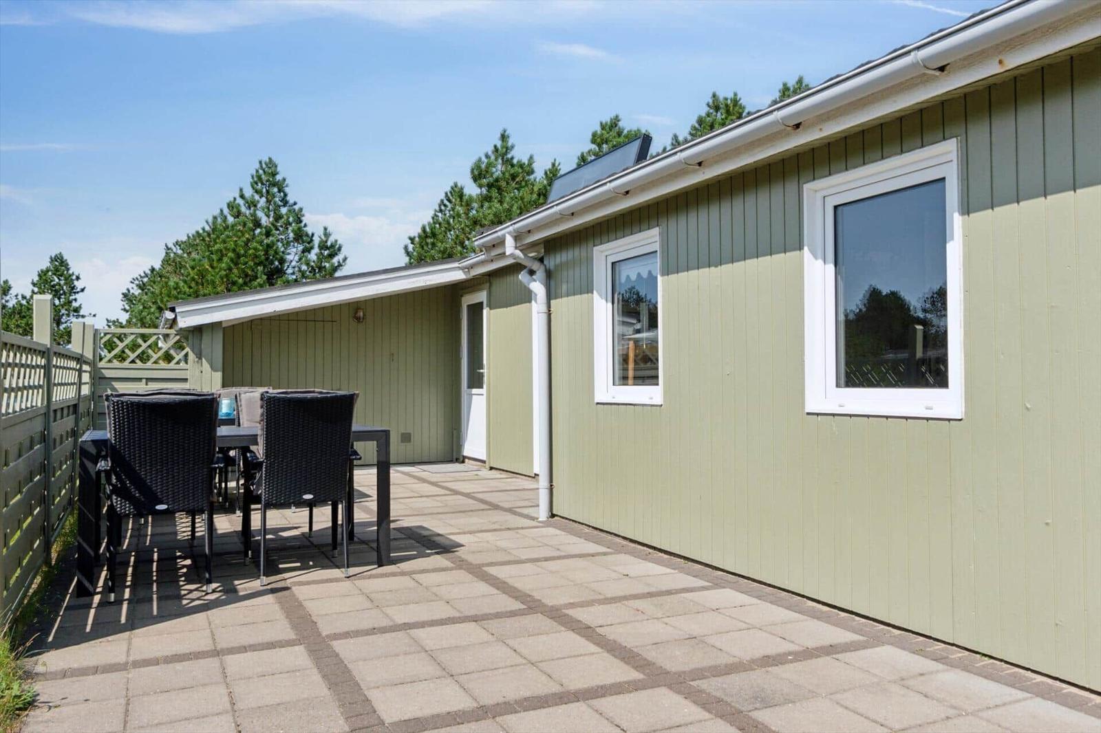 Terrasse mit Tisch und Stühlen neben einem hellgrünen Ferienhaus.