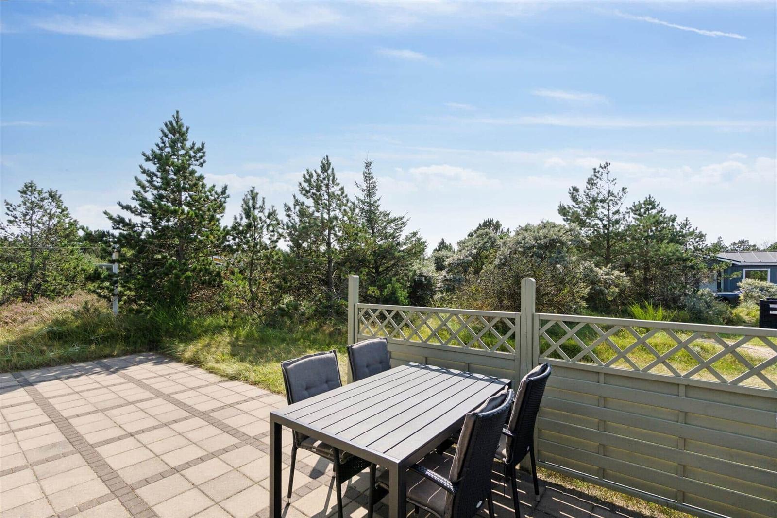 Terrasse mit Tisch und Stühlen, Blick auf Bäume und Himmel.