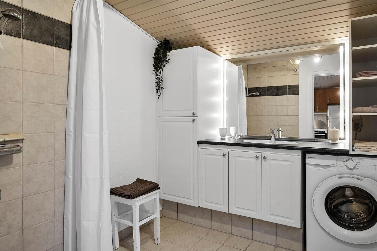 Badezimmer mit Dusche, Waschmaschine und Spiegelschrank.