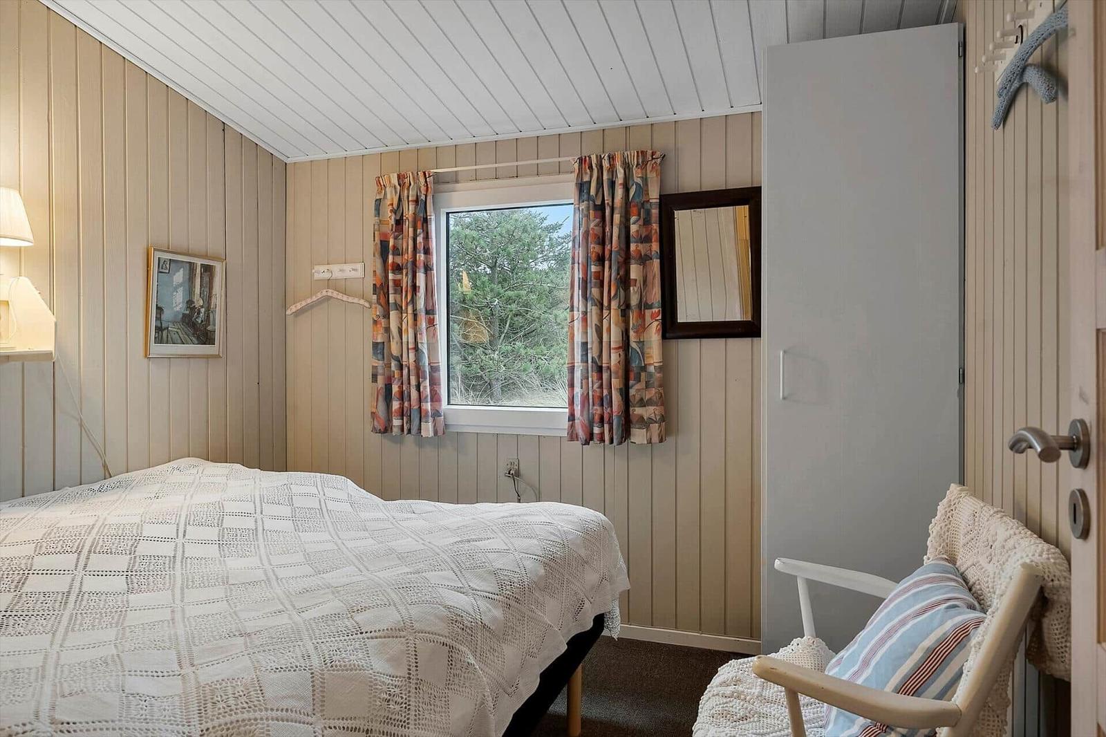 Schlafzimmer mit Bett, Fenster und Stuhl. Wandverkleidung und Vorhänge.