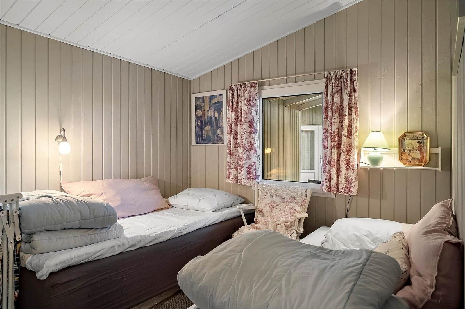 Zwei Betten mit Bettwäsche, Fenster mit Vorhängen, Wandlampen und Bild an der Wand.
