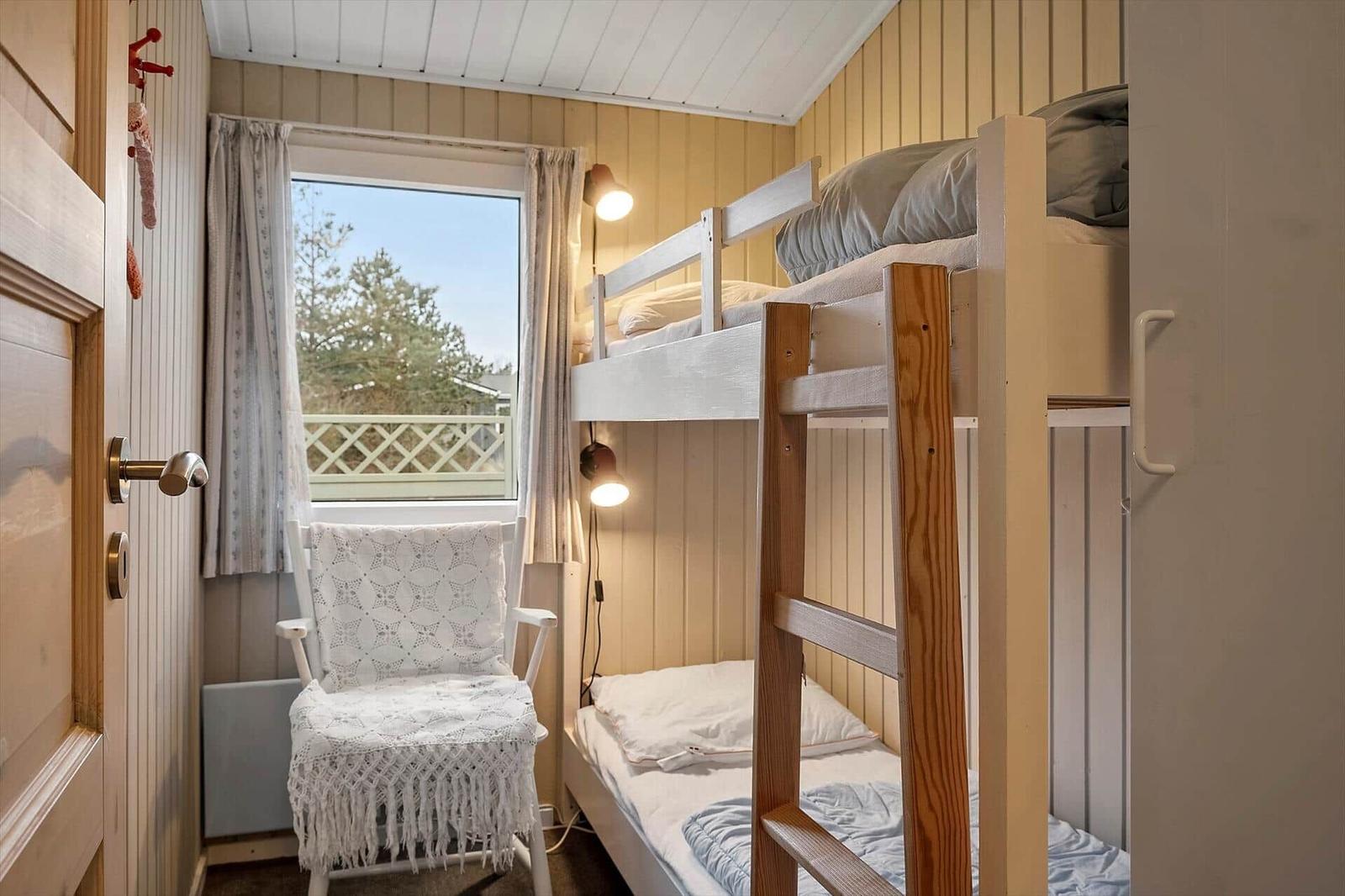 Zimmer mit Doppelstockbett, Stuhl und Fenster mit Blick auf Balkon.
