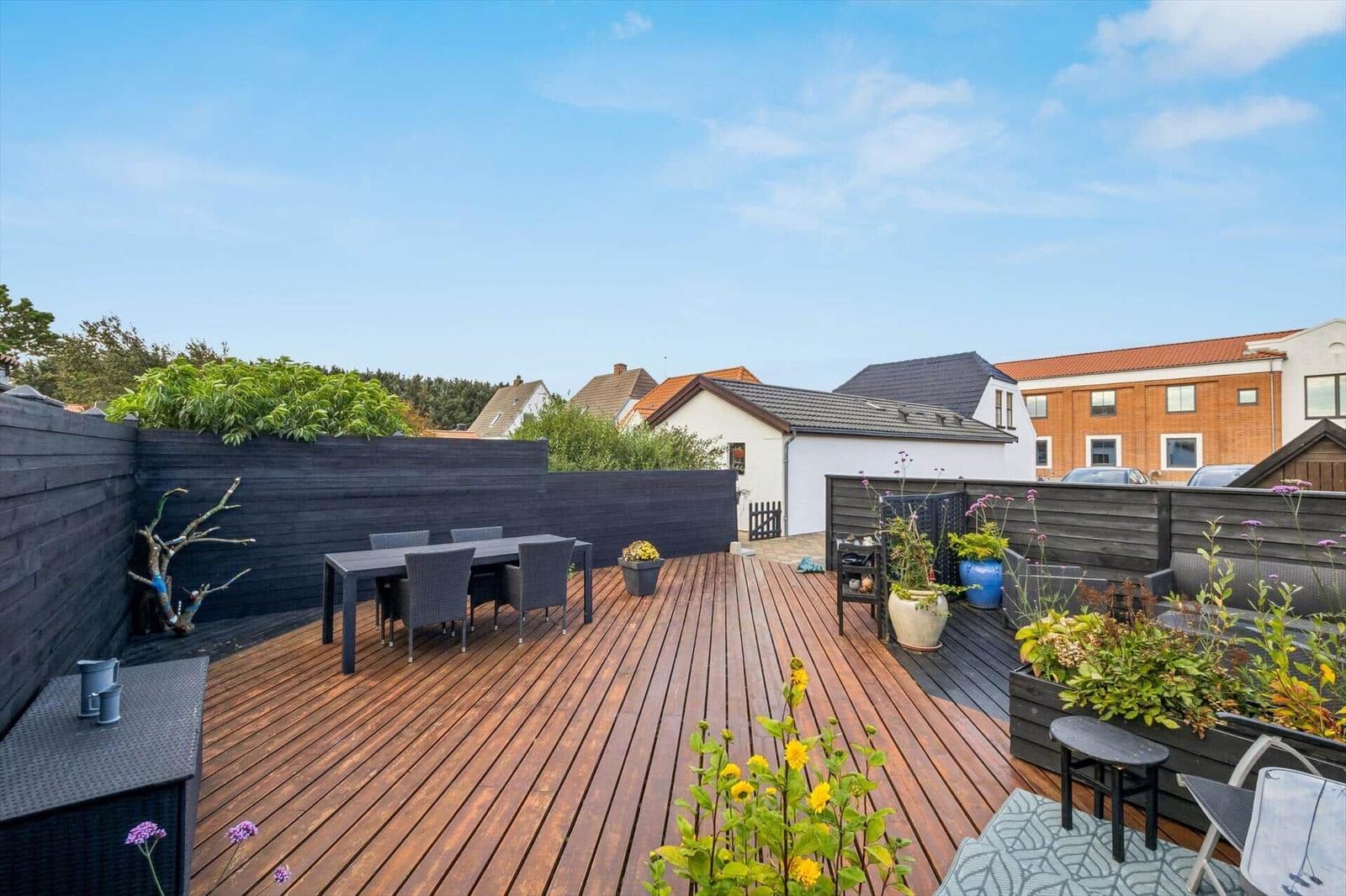 Deck with wooden planks, garden furniture, and plants. View of neighboring houses.
