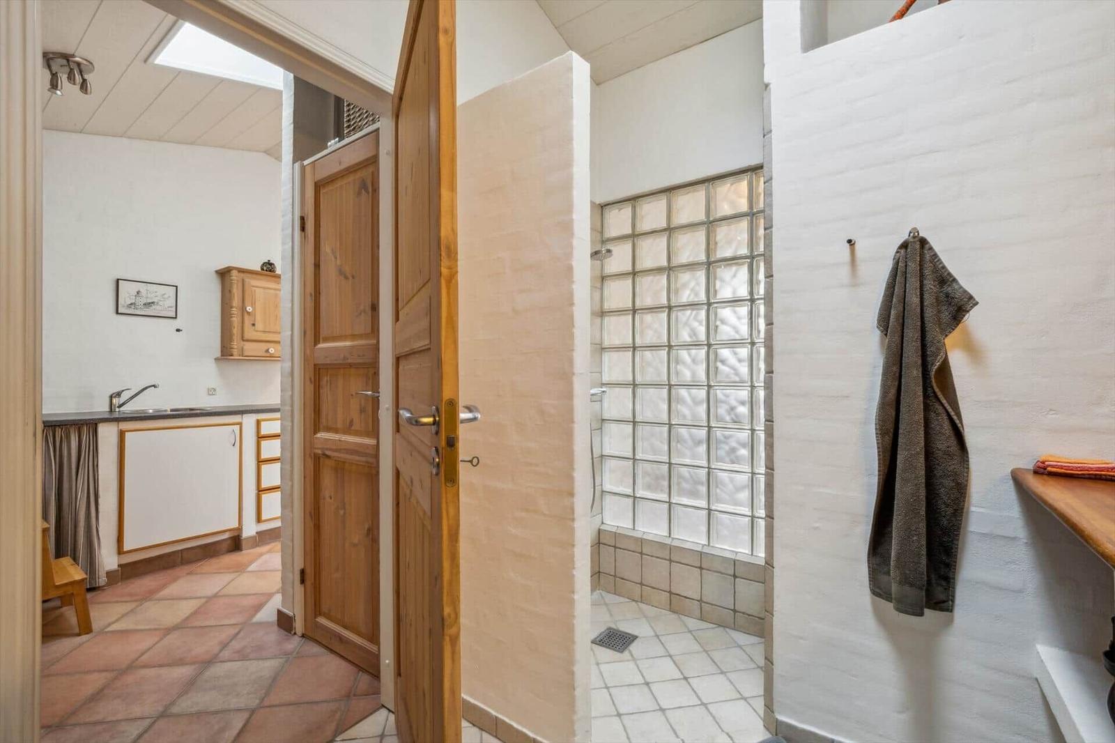 Bathroom with shower and adjacent kitchen with wooden doors.