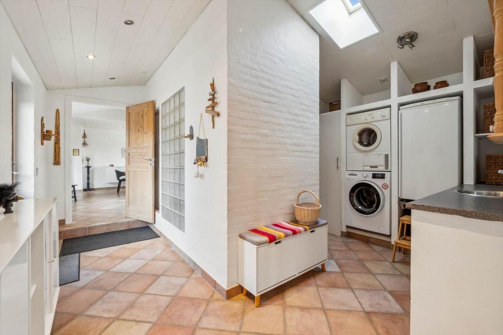 Entrance area with washing machine, fridge, and bench with basket.