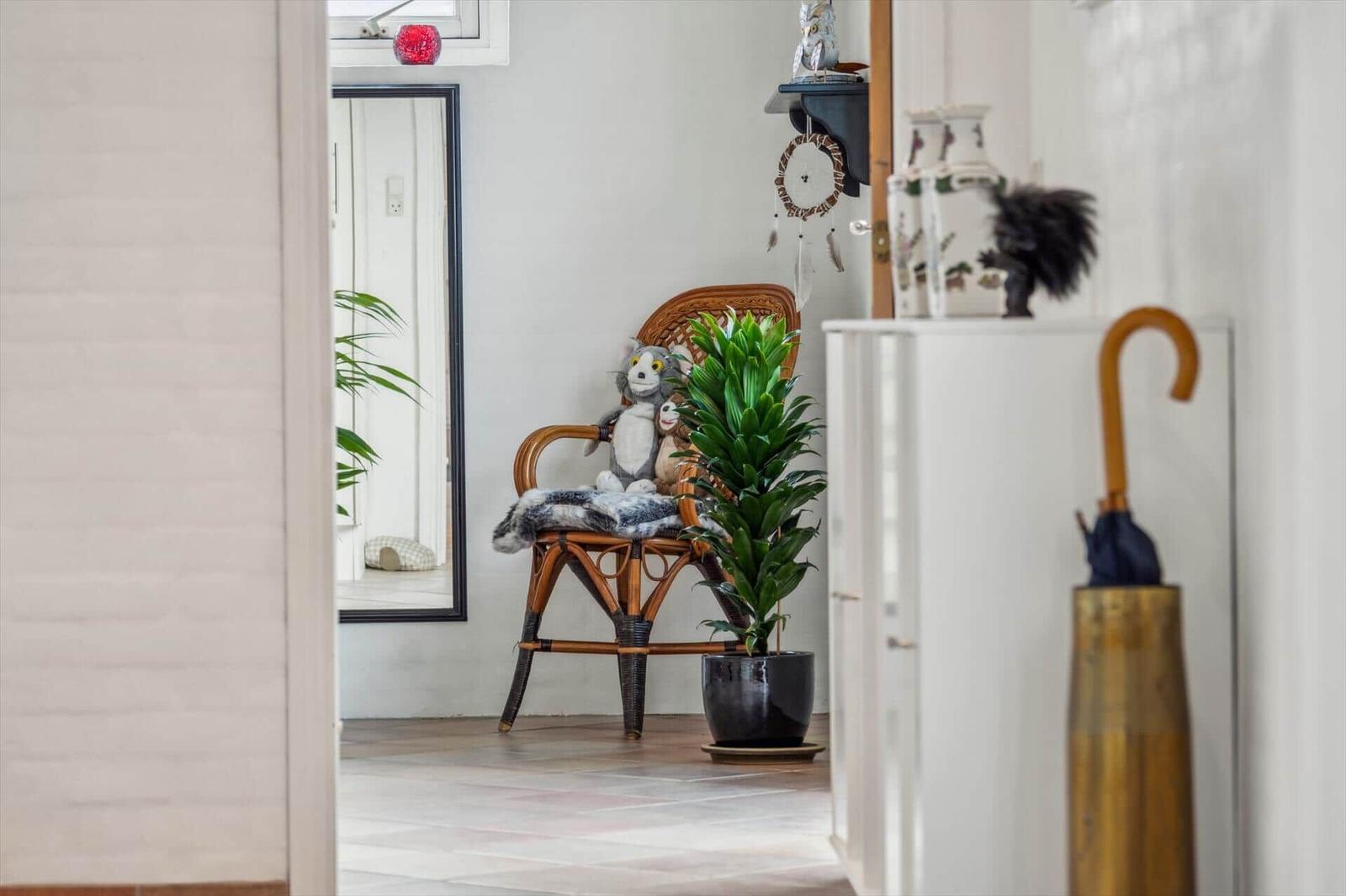 A room with chair, plant, and mirror. Shelf with vases and decor.