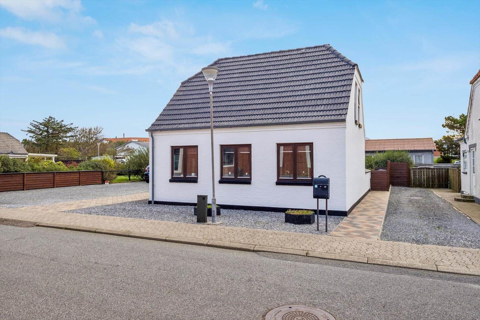 A white house with brown windows and a gray roof stands on a street.