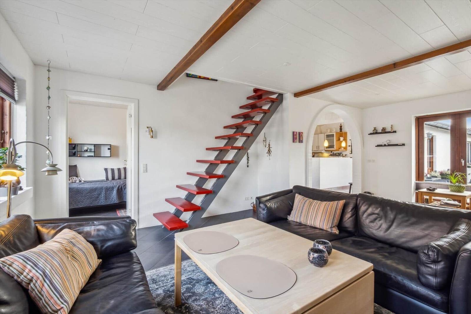 Living room with leather sofa, wooden table, and red staircase to upper level.