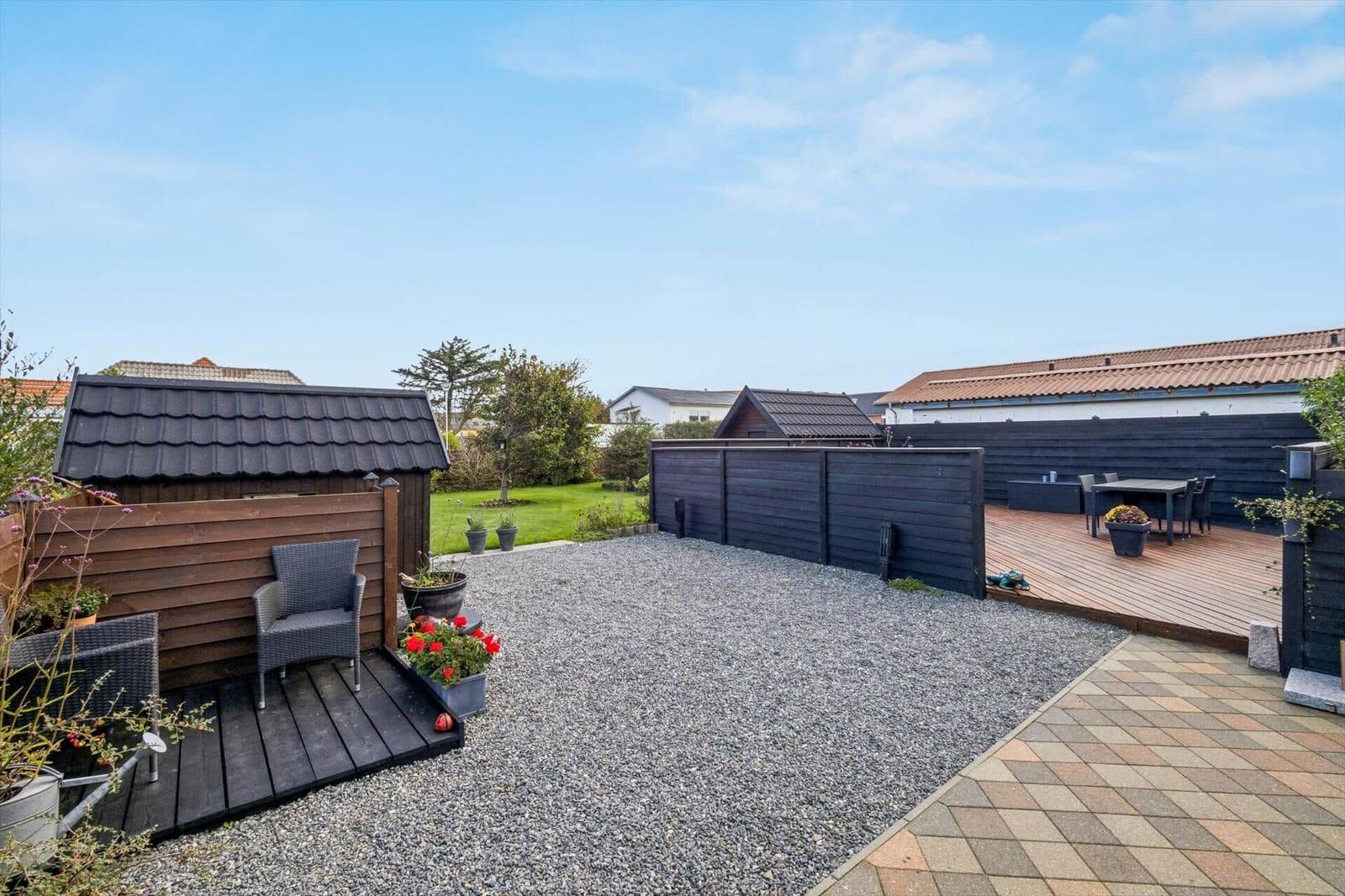 Rear yard with wooden deck, gravel area, and shed under blue sky.