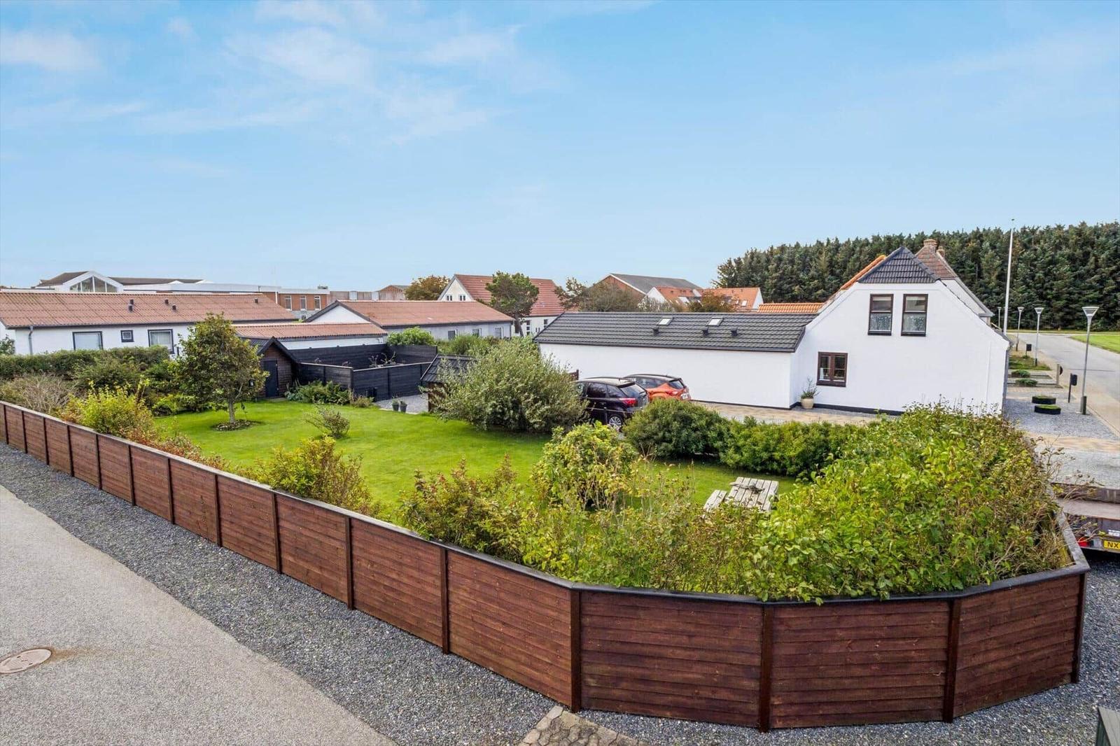 House with garden, wooden border, and paved path. Backyard with trees and road.