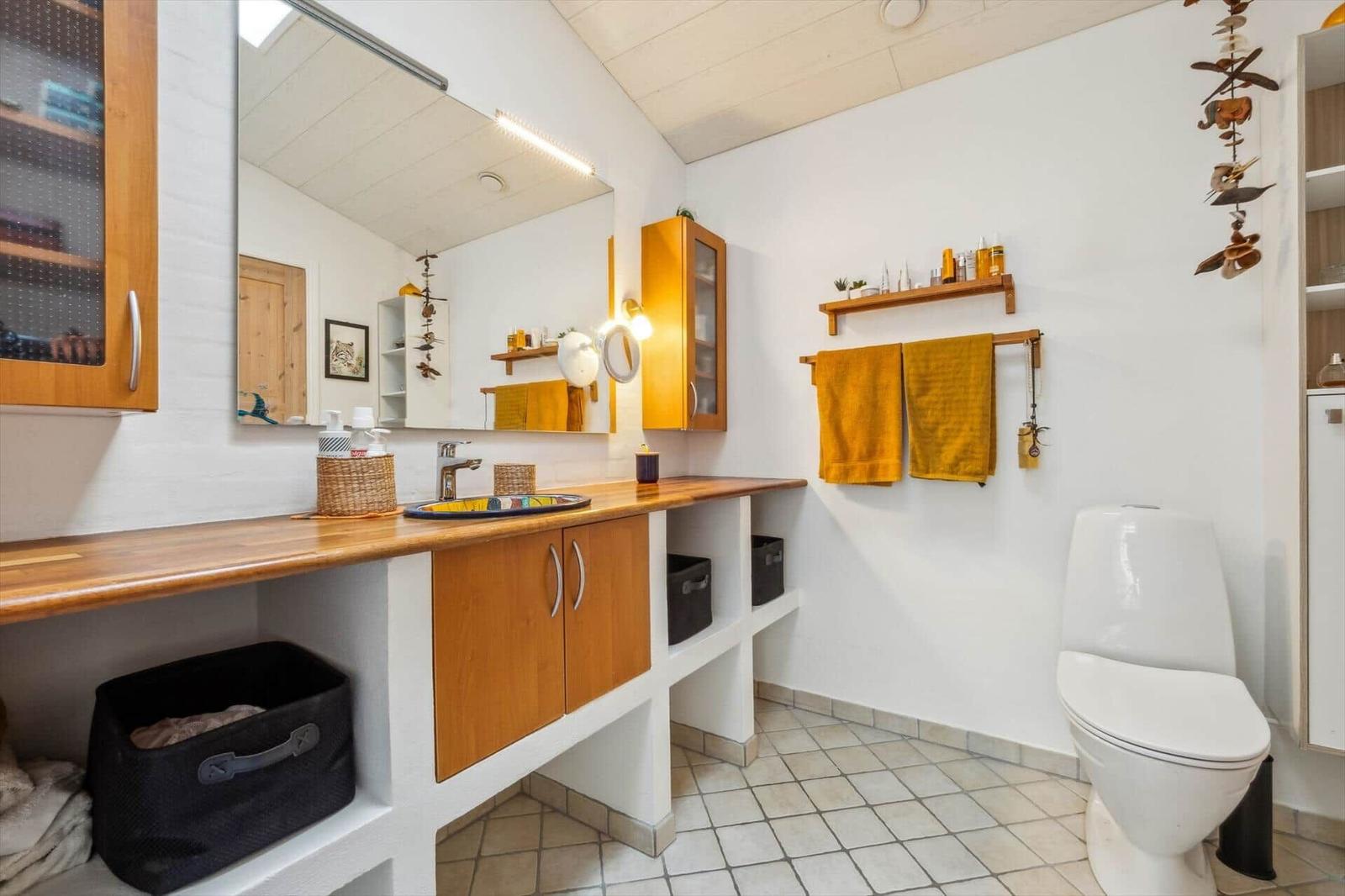 Bathroom with wooden sink counter, mirror, and toilet. Yellow towels hang on the wall.