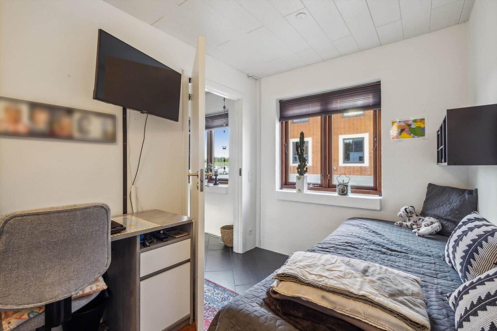 Bedroom with bed, TV, and window overlooking a house.