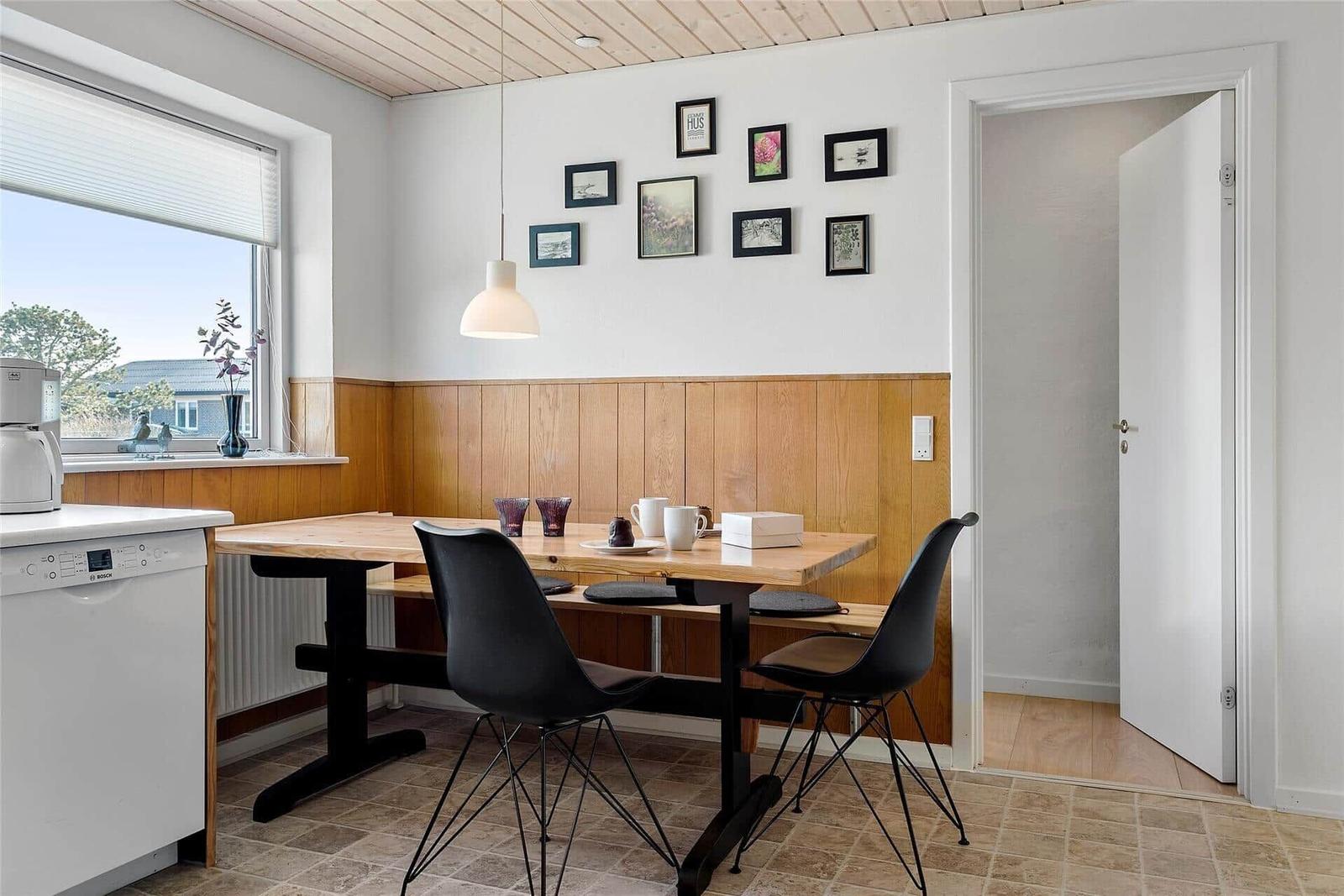 Essbereich mit Tisch, Stühlen und Fensterblick. Wand mit Bildern und Holzverkleidung.