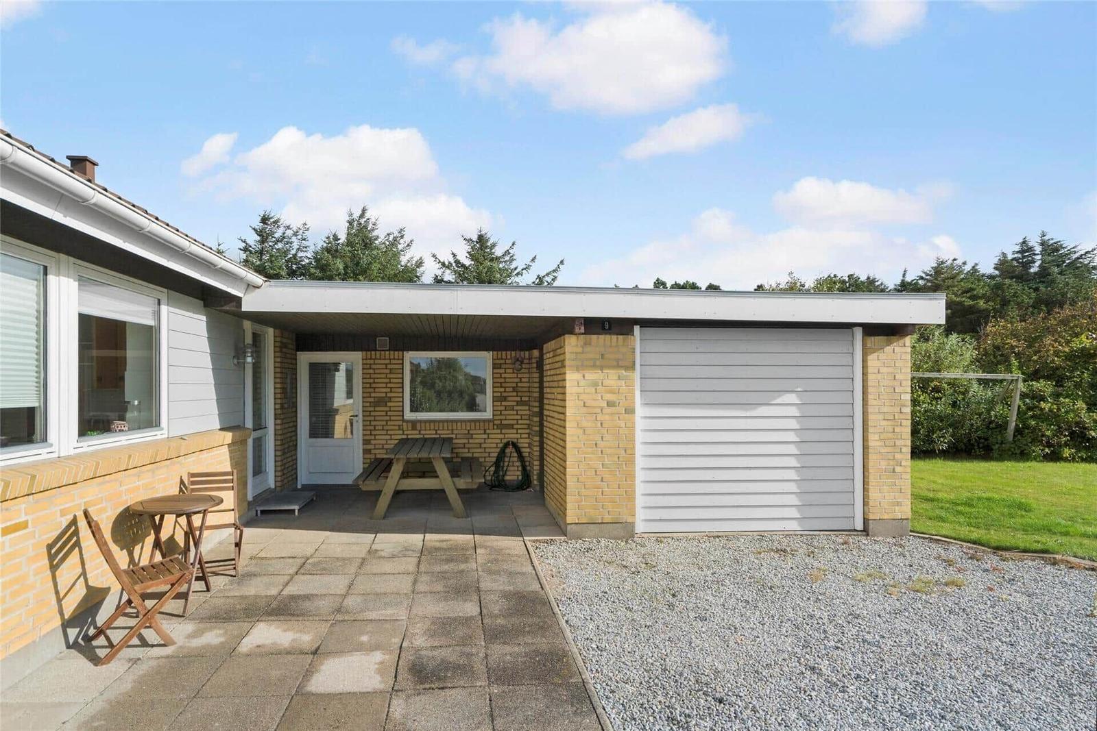 Haus mit Garage, Terrasse und Gartenbereich mit Tisch und Stühlen.