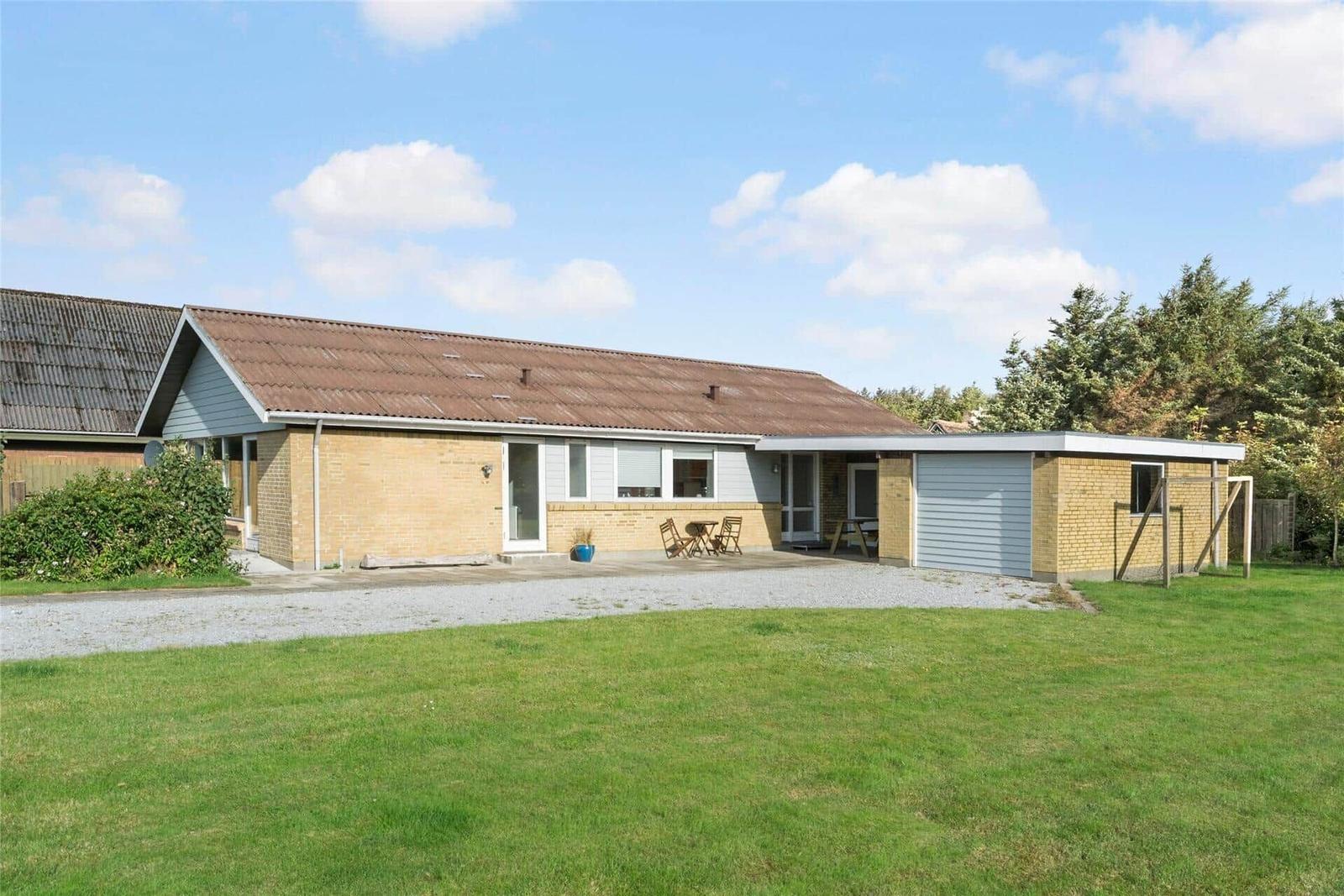 Ein Haus mit Garage und Terrasse im Garten unter blauem Himmel.