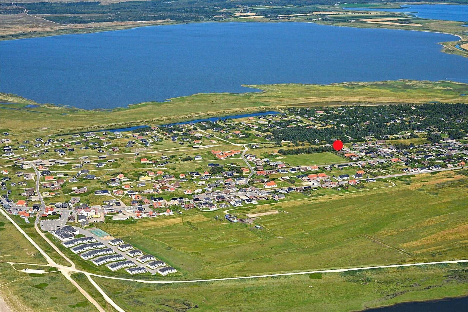 Luftbild einer kleinen Ortschaft am Ufer eines Sees mit grünen Wiesen und Häusern.