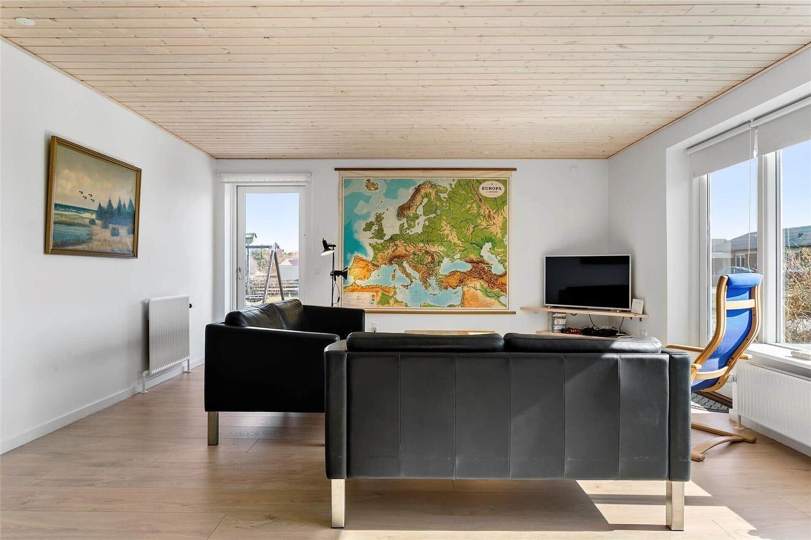 Wohnzimmer mit schwarzen Ledersofas, Holzboden und Europa-Karte an der Wand.
