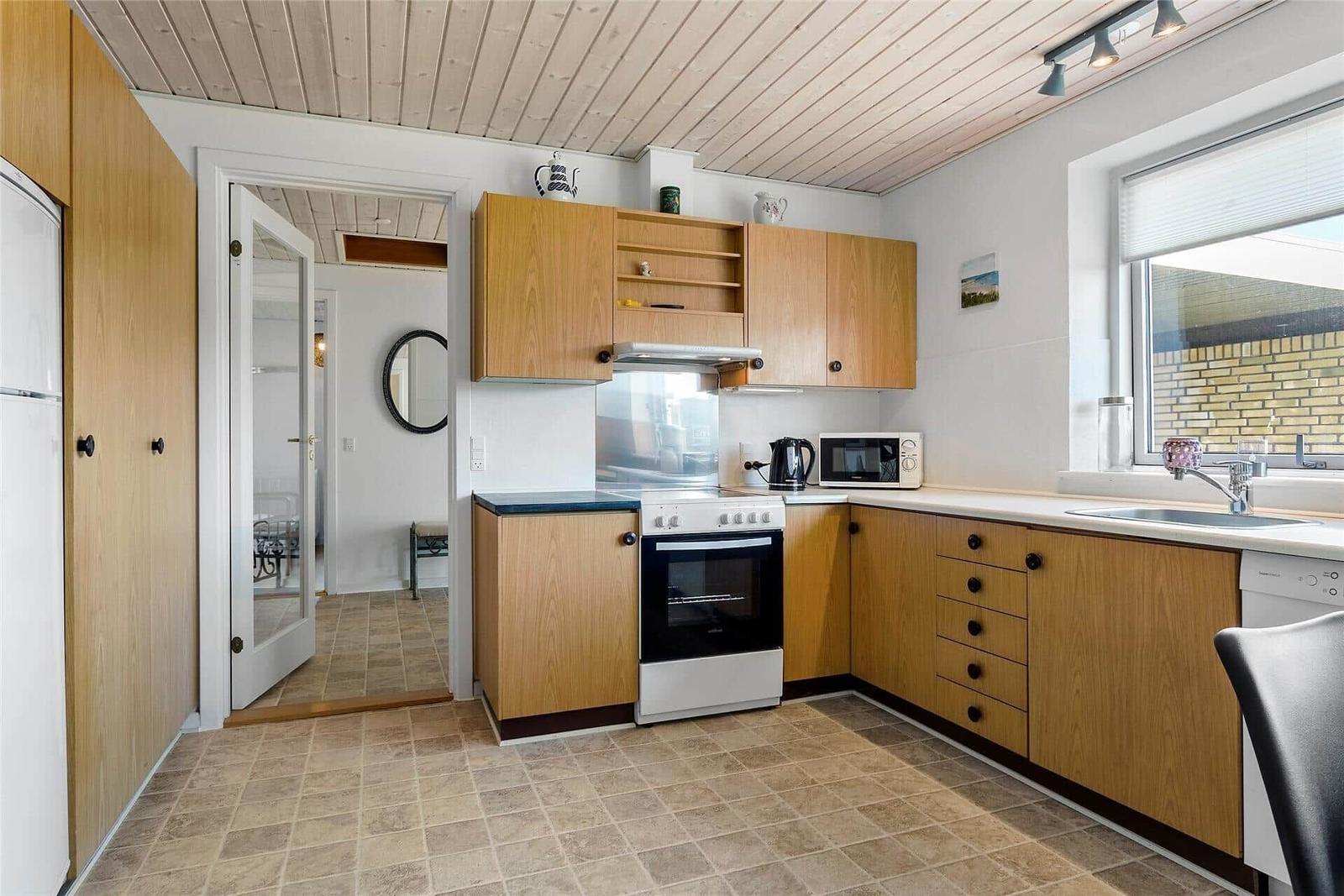 Küche mit Holzschränken, Herd, Spüle und Fenster