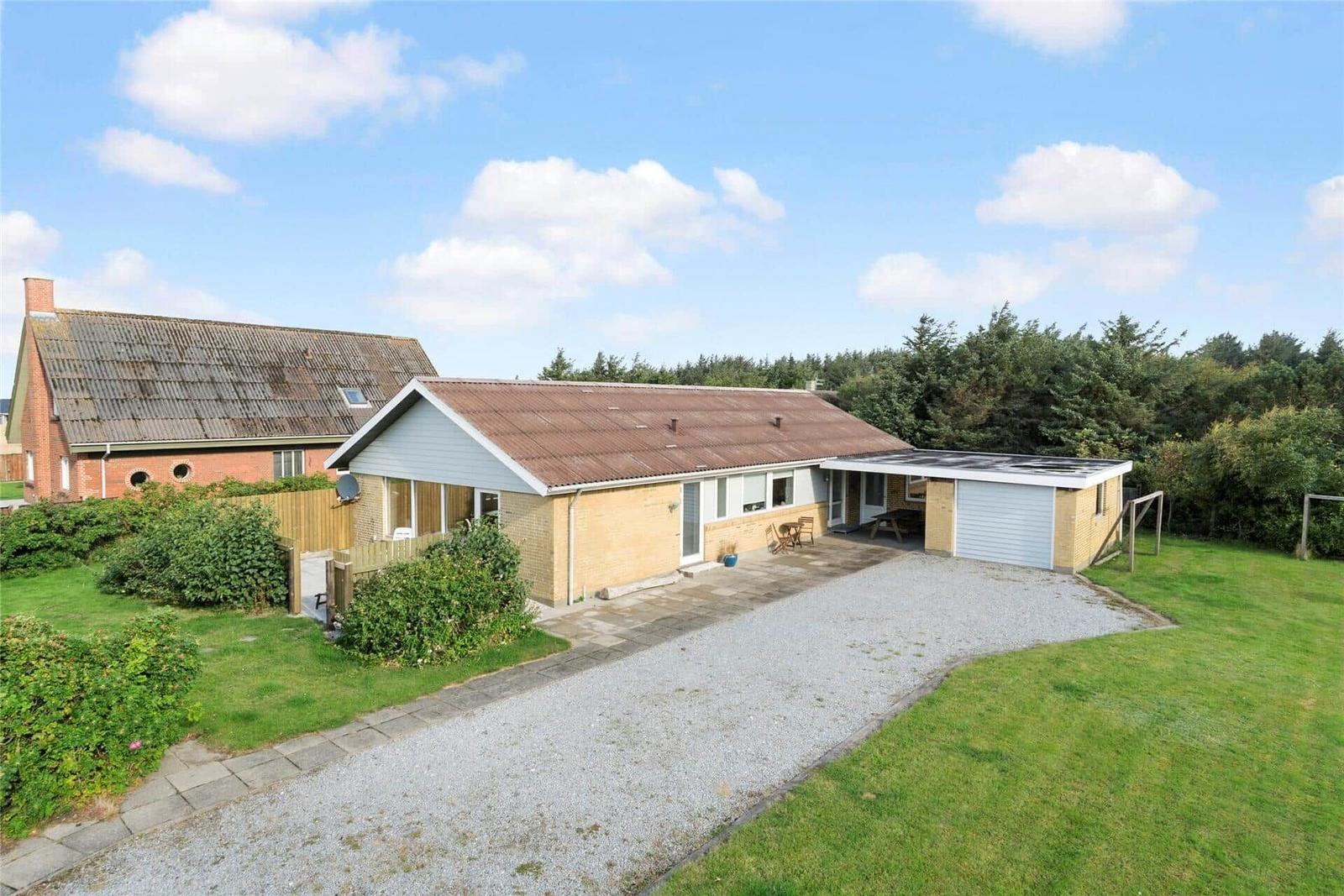Ein Haus mit Garten, Garage und Terrasse unter blauem Himmel.