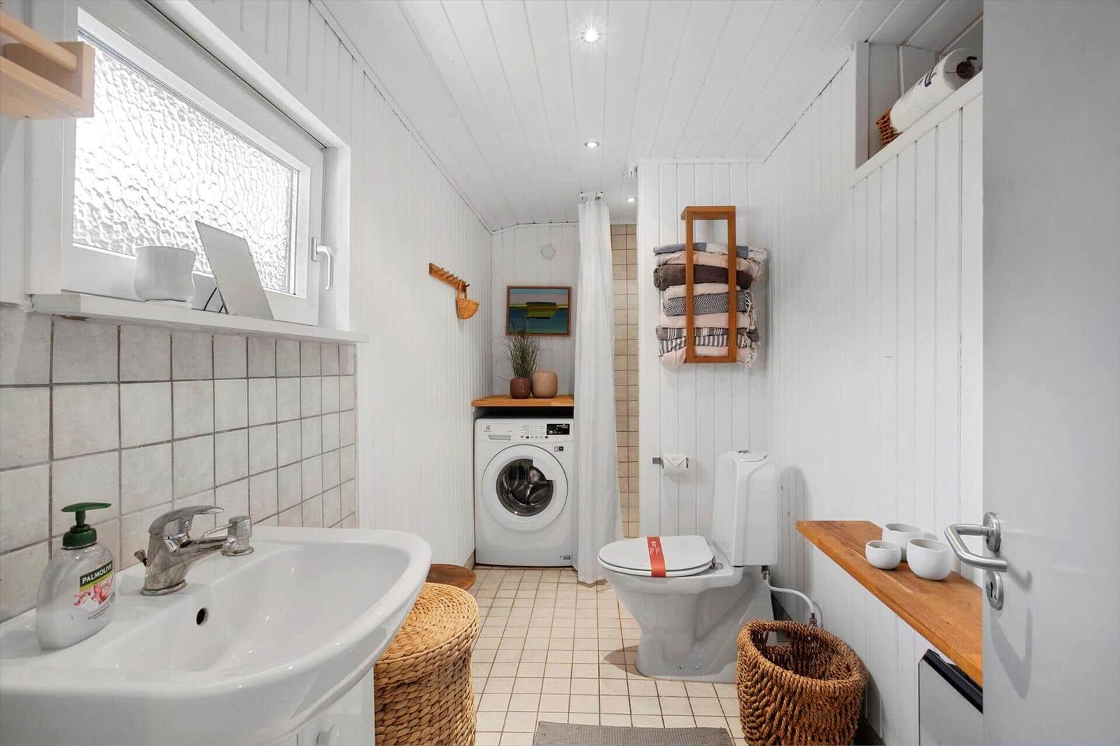 Bathroom with washing machine, toilet, and shower. Wooden shelves and baskets.