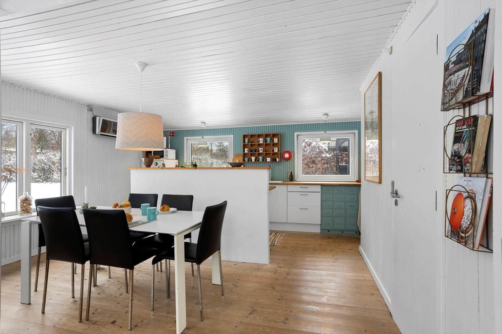 Dining area with table and chairs, kitchen with countertop and windows.