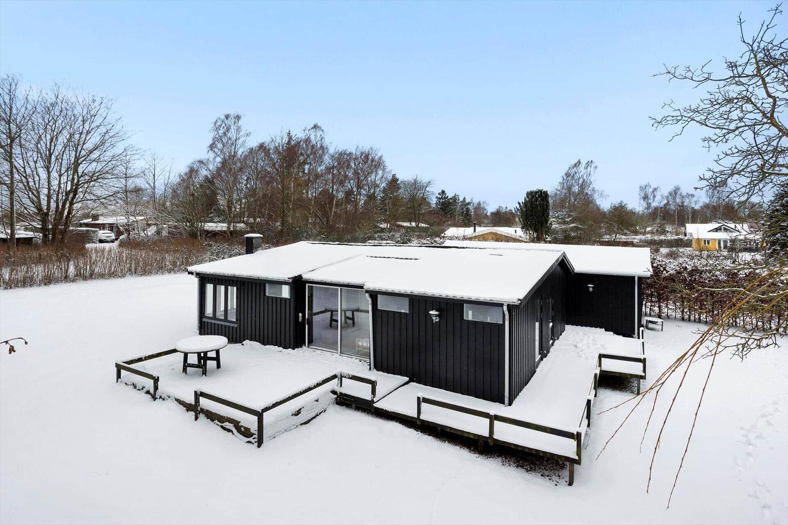Black house with snow-covered roof and terrace in winter.