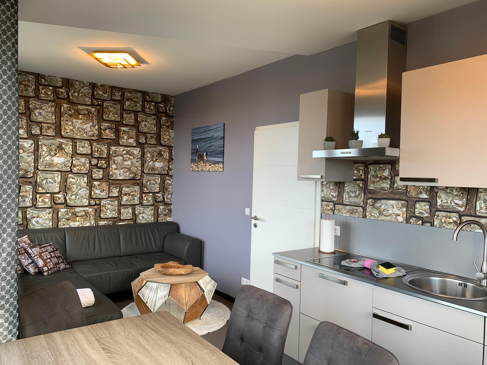 Wohnbereich mit Sofa, Esstisch und Küchenzeile mit Arbeitsplatte und Spüle.