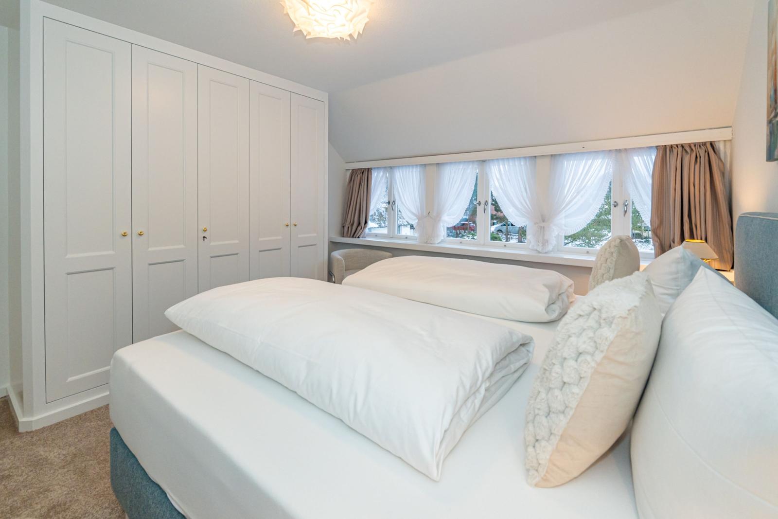 Schlafzimmer mit Doppelbett, Kleiderschrank und Fenster mit Vorhängen.