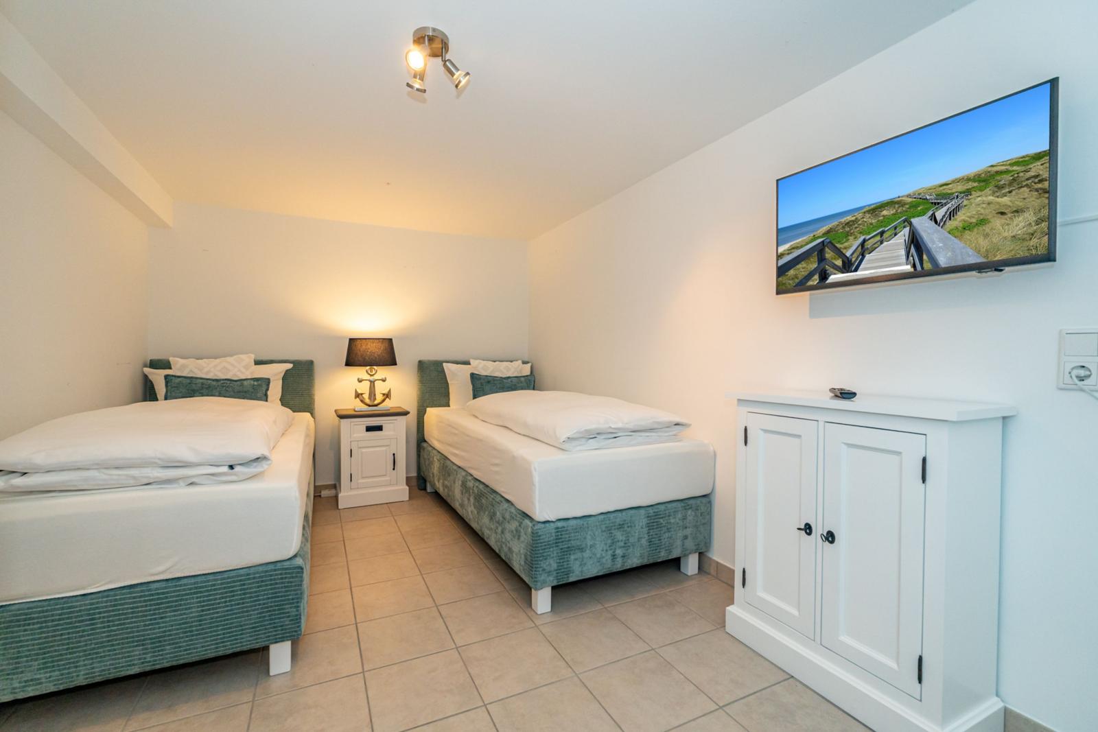 Zwei Einzelbetten, Nachttisch, Fernseher und Schrank im Zimmer.