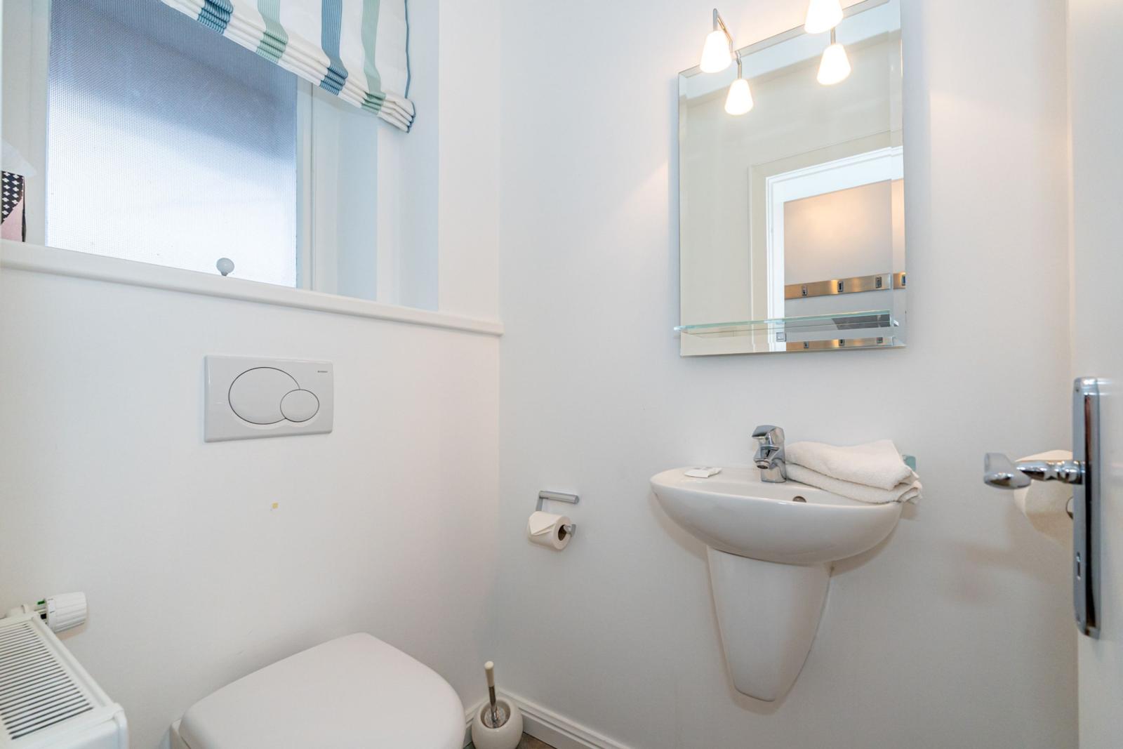 Badezimmer mit Waschbecken, Spiegel und Toilette. Fenster mit Rollladen.