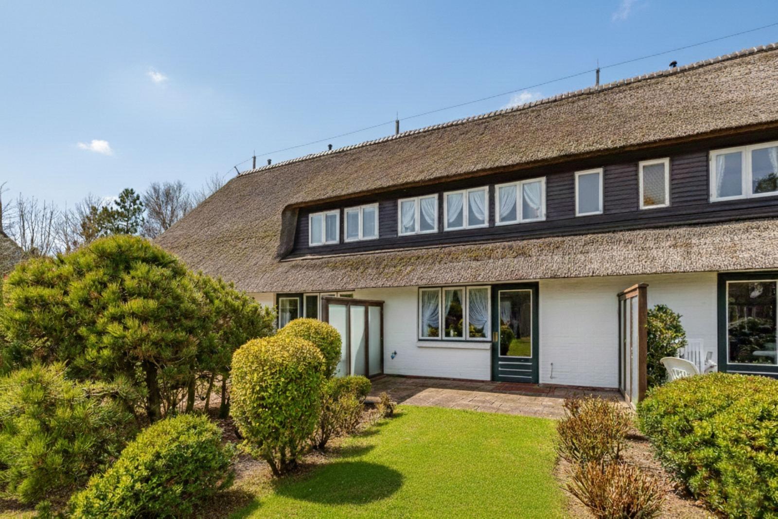 Haus mit Strohdach, weißer Fassade und grünem Garten.