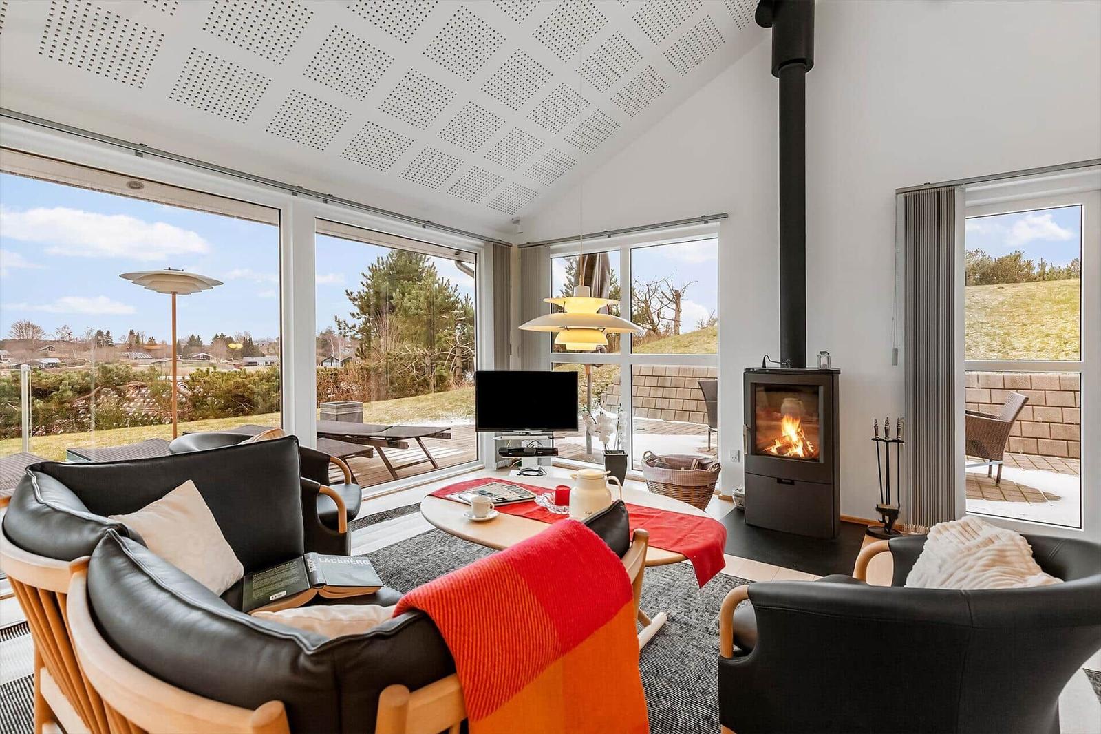 Wohnzimmer mit Kamin, Sitzgruppe und großflächigen Fenstern zur Aussicht.