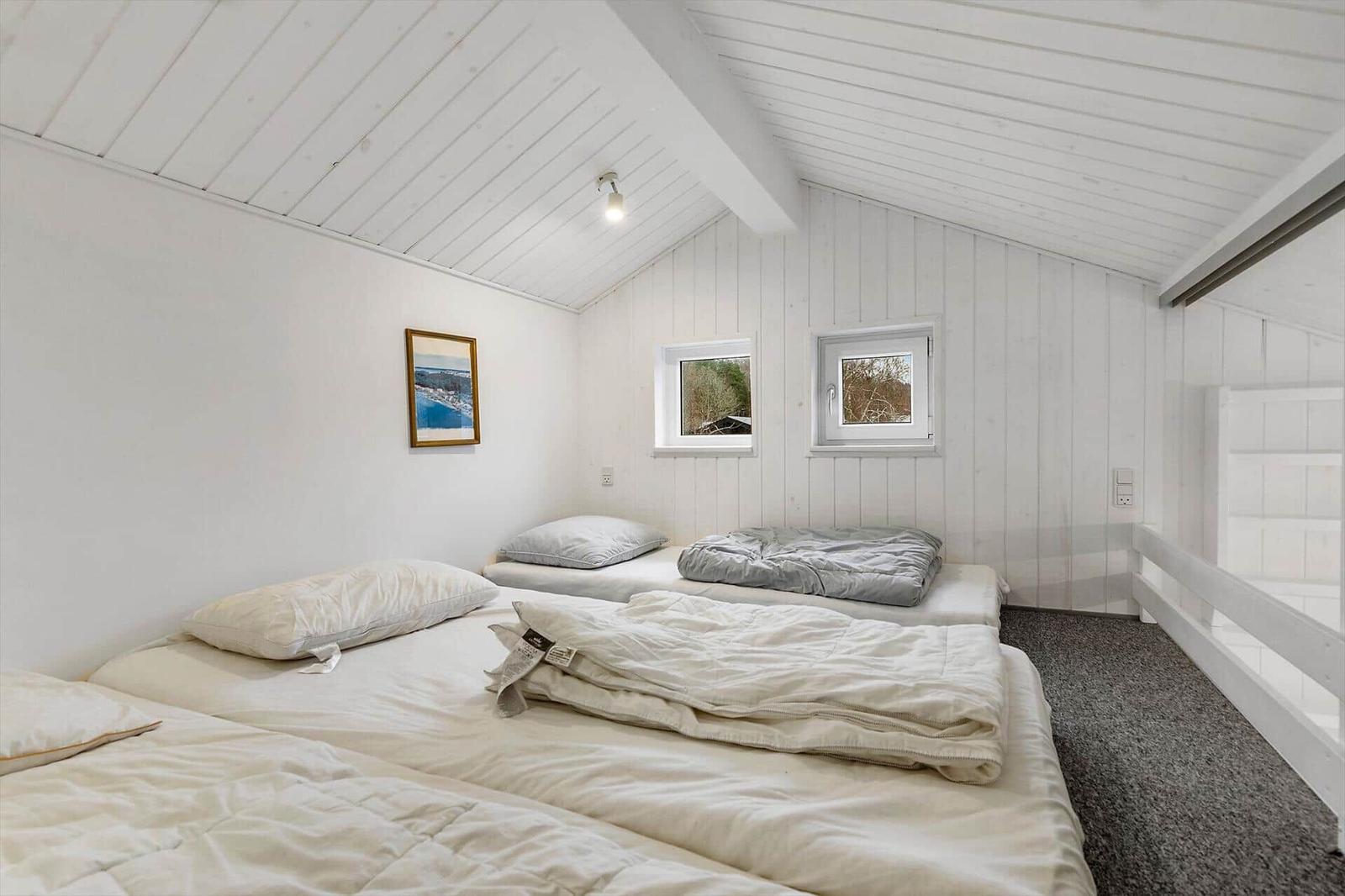 Zimmer mit zwei Betten, weißen Wänden und zwei Fenstern. Decke mit Holzverkleidung.