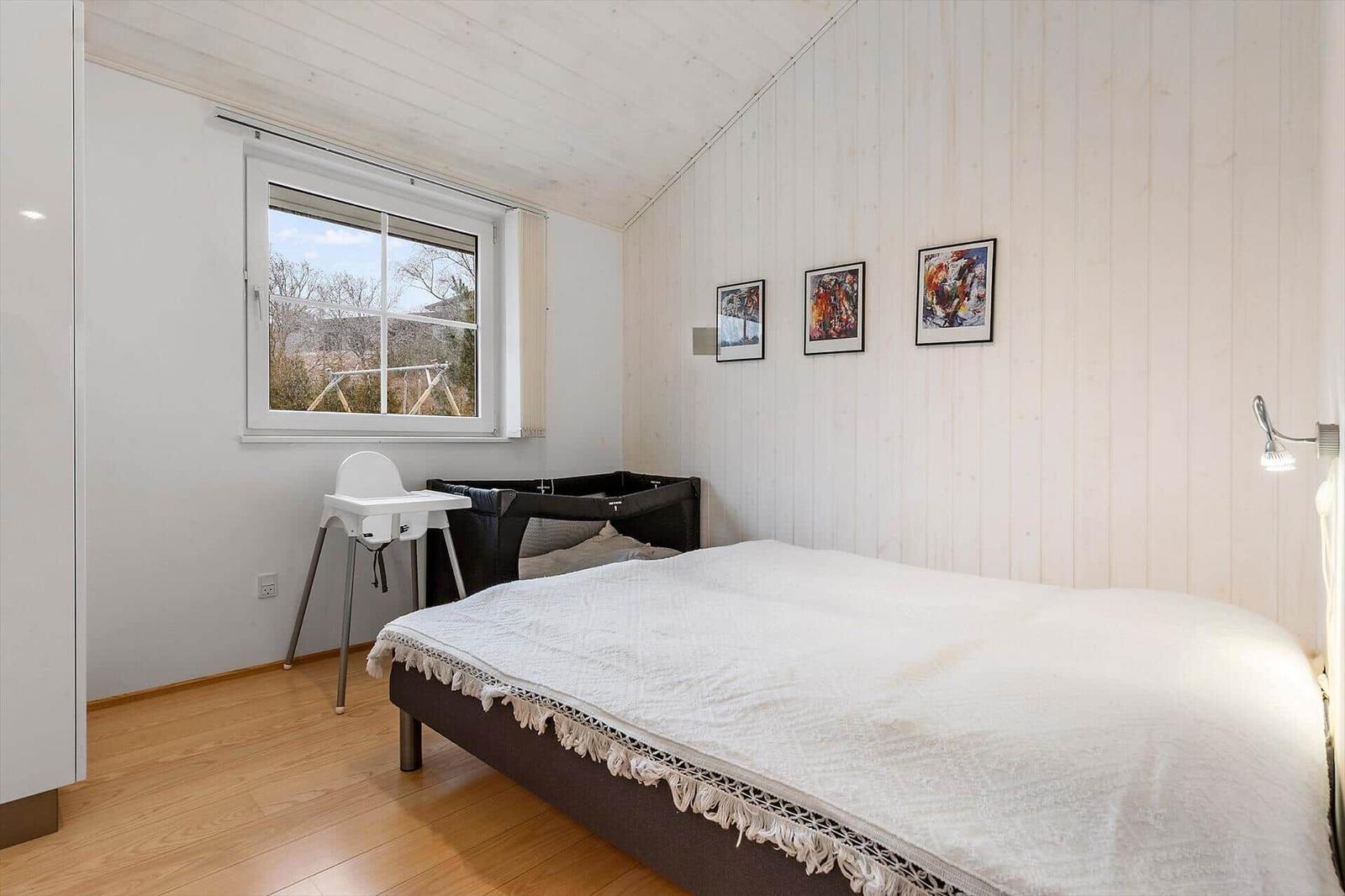 Schlafzimmer mit Bett, Kinderbett und Hochstuhl. Holzwand und Fenster mit Blick.