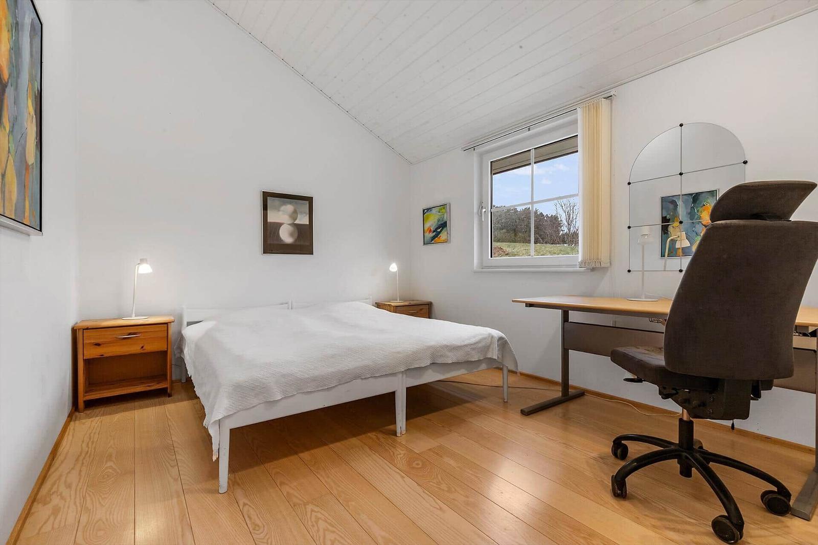 Schlafzimmer mit Bett, Schreibtisch und Fenster mit Blick auf Landschaft.