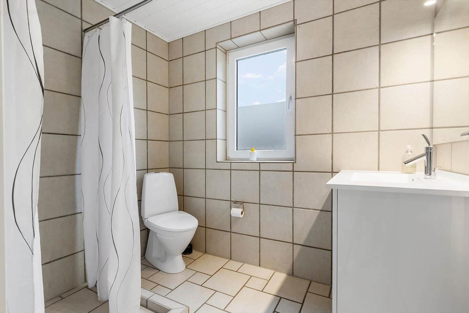 Badezimmer mit Toilette, Waschbecken und Dusche. Fenster mit Blick nach draußen.
