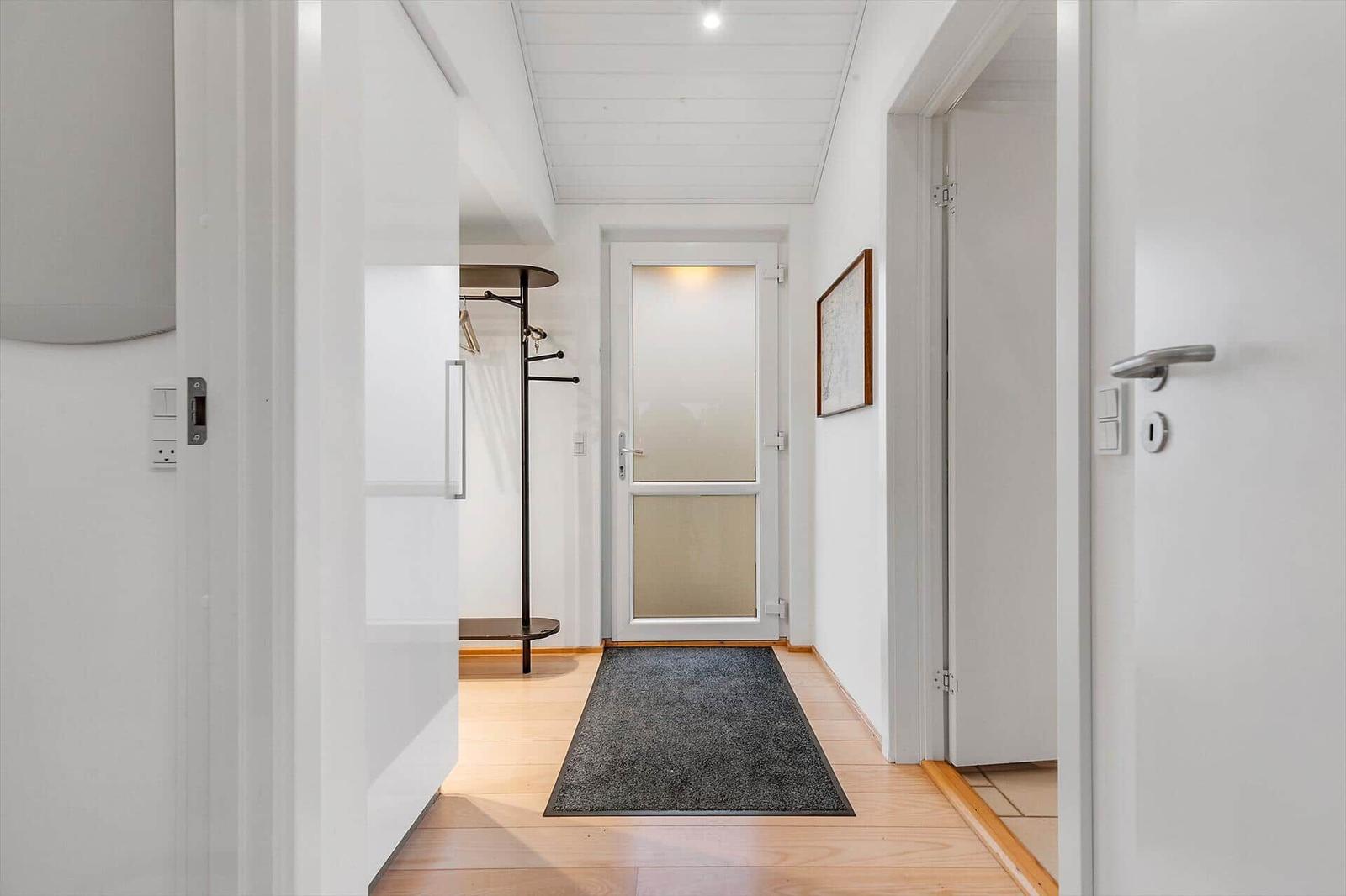Flur mit Holzboden, Teppich und Garderobe. Tür mit Glasfenster und Wandbild.