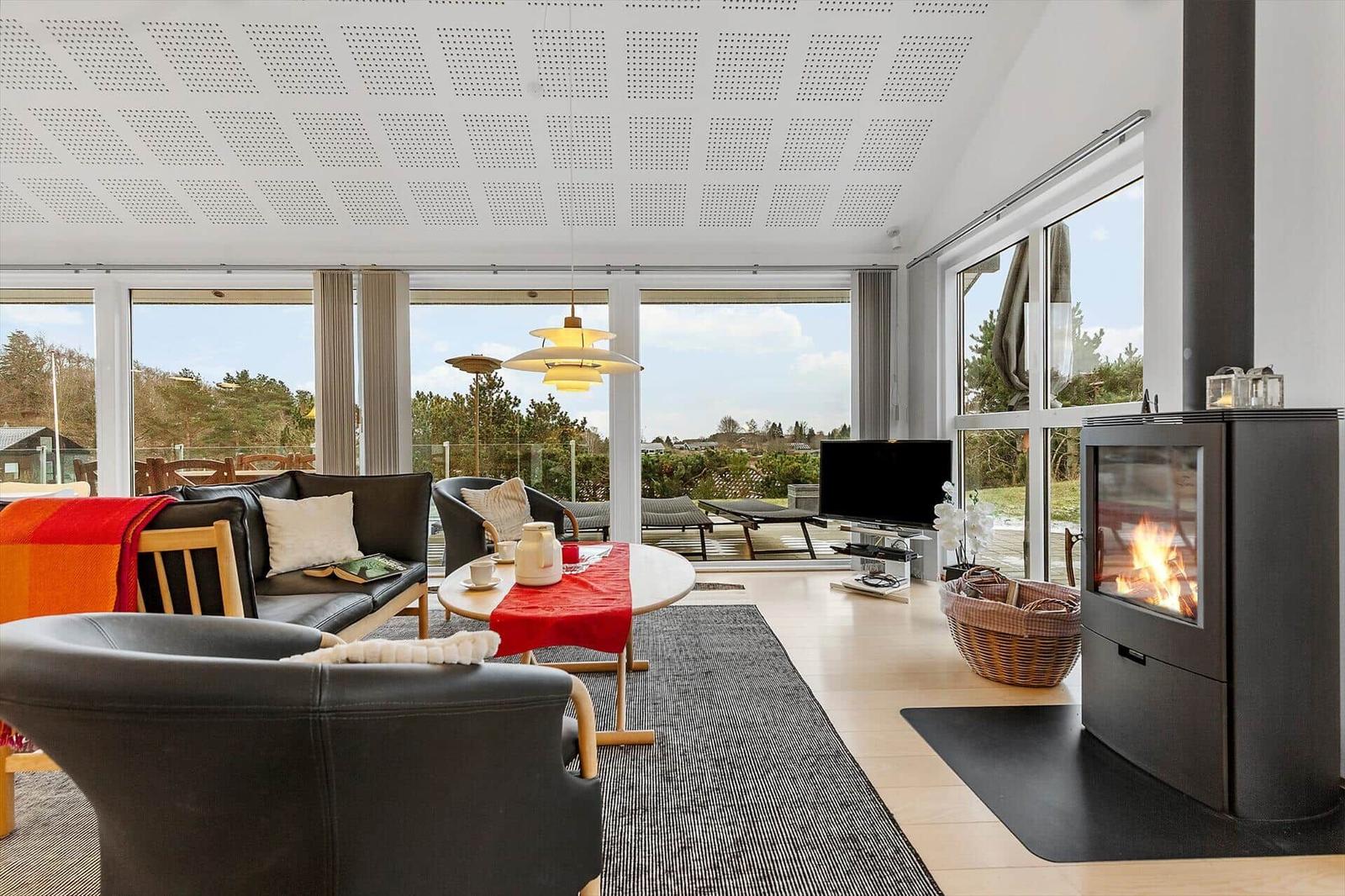 Wohnzimmer mit Kamin, Sofa und großem Fensterblick auf die Landschaft.
