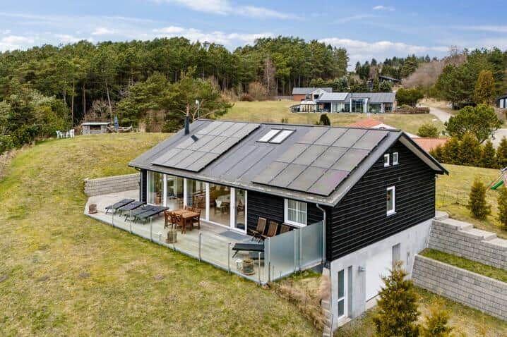 Schwarzes Haus mit Terrasse und Solarpanel auf grünem Grundstück.