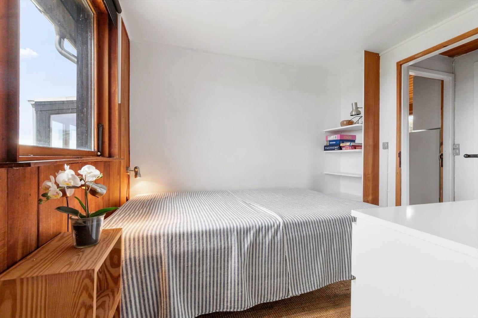 Schlafzimmer mit Bett, Fenster und Regal. Holzwände und weißer Schrank.