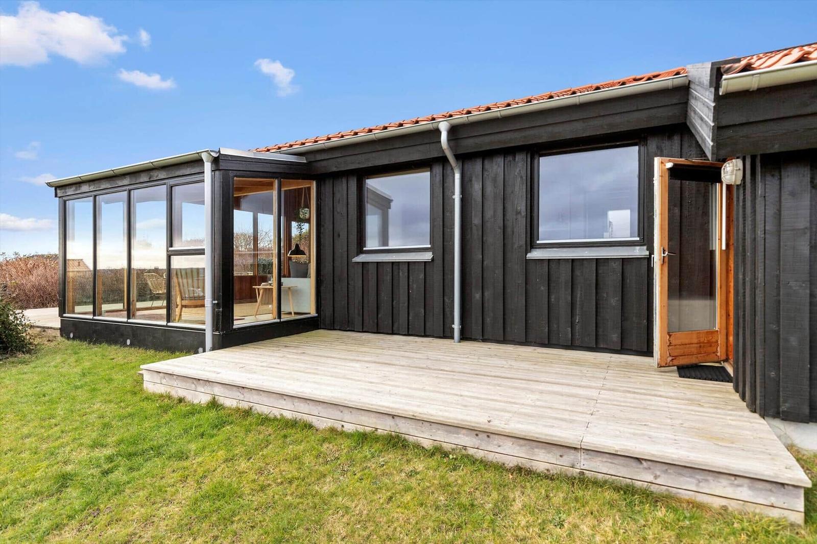 Holzhaus mit Terrasse und Glasveranda. Tür offen. Grasfläche vor dem Haus.
