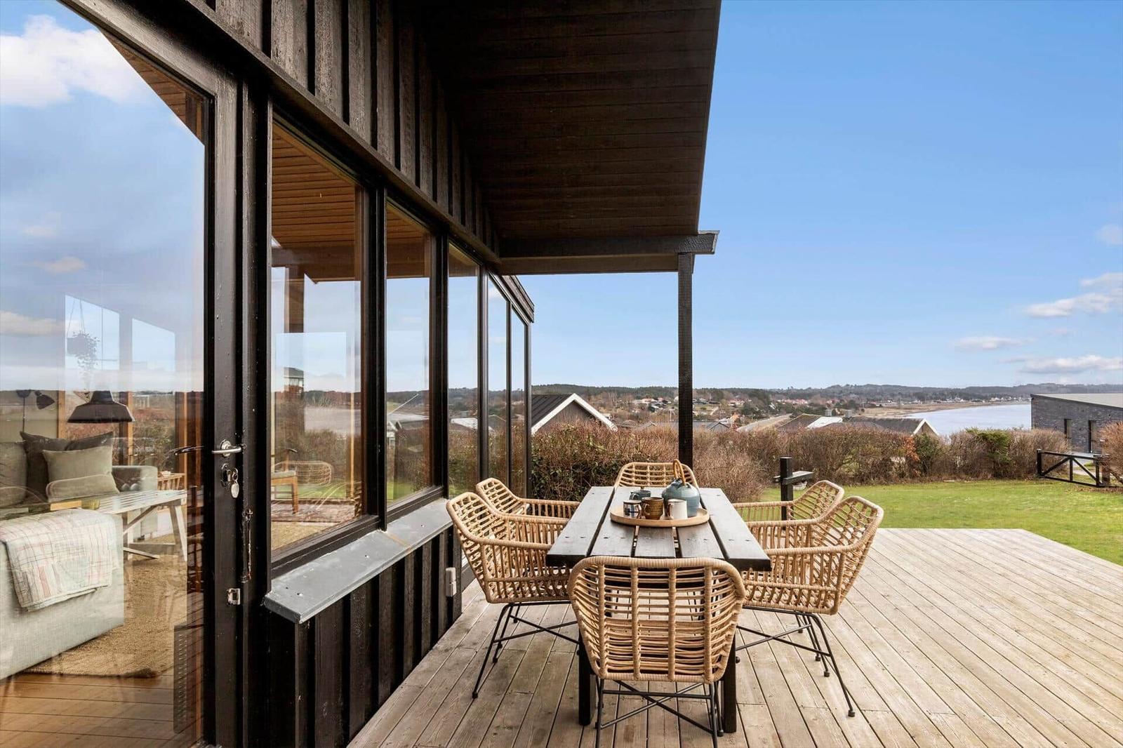 Terrasse mit Tisch und Stühlen, Blick auf Landschaft und Wasser.