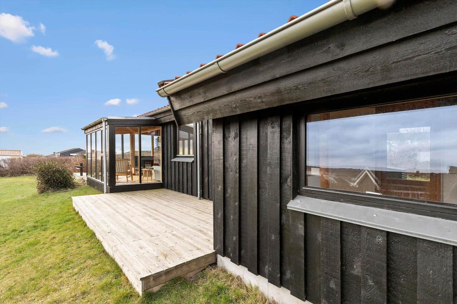Holzhaus mit Terrasse und Glasveranda. Grünfläche und klarer Himmel.