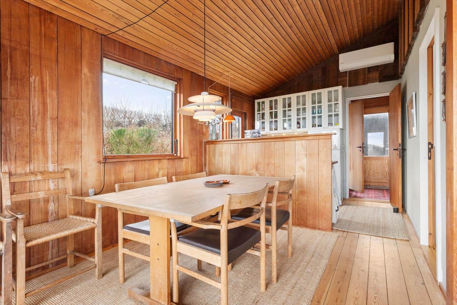 Esszimmer mit Holztisch, Stühlen und Küchenbereich. Holzwände und -decke.