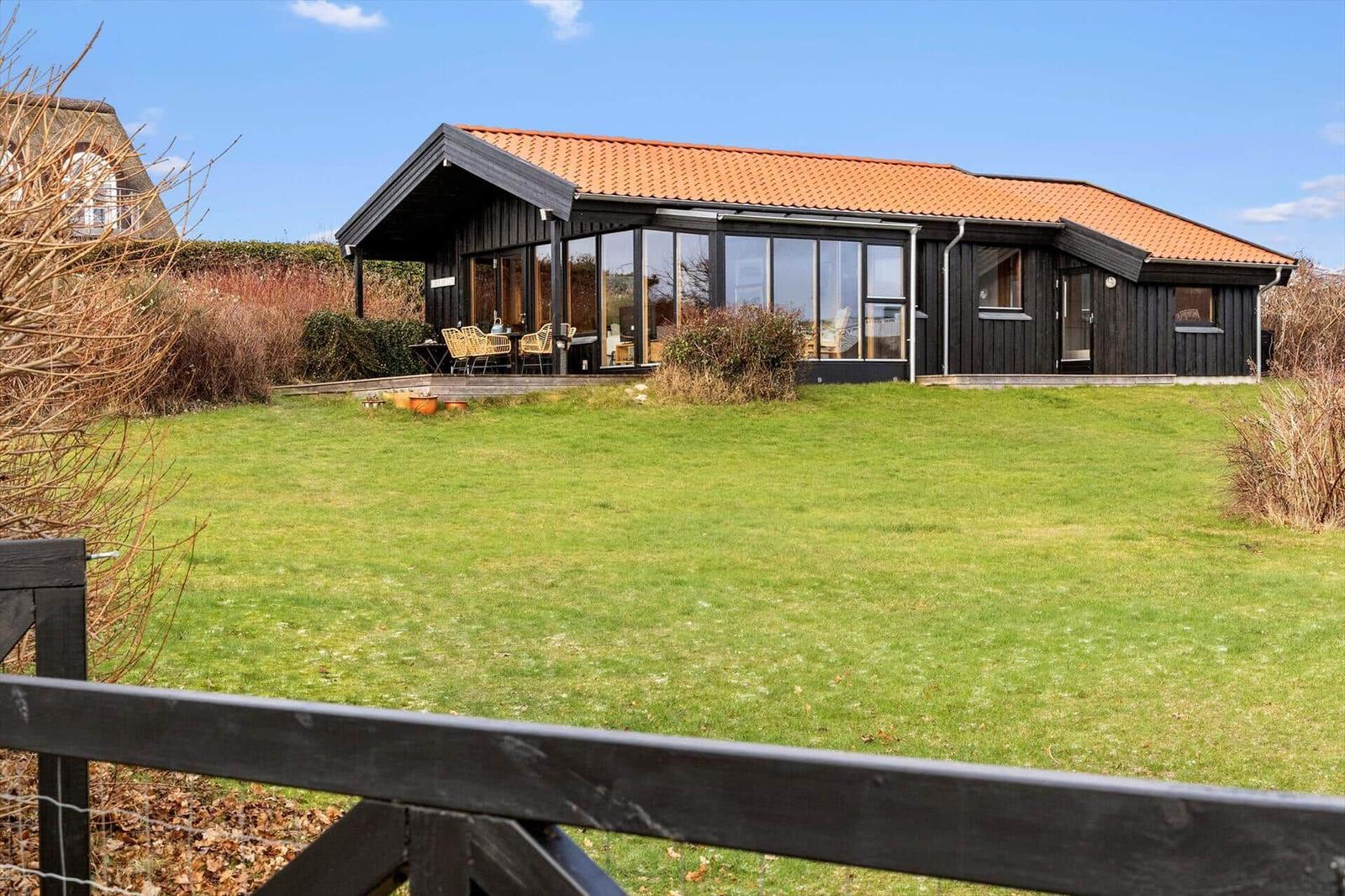 Moderne Villa mit großem Garten und Terrasse. Holzverkleidung und orangefarbener Dachziegel.