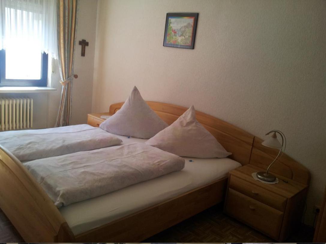 Ein Schlafzimmer mit Holzbett, Nachttisch und Fenster.